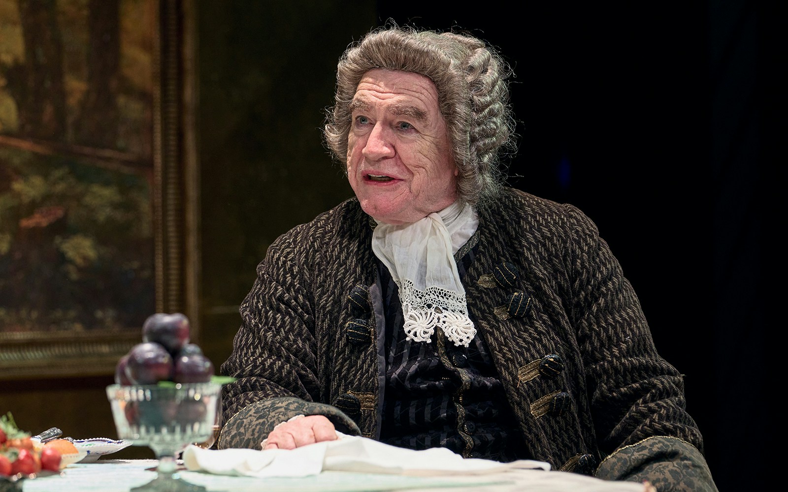 Actor in period costume seated at a table with fruit, related to The Score.