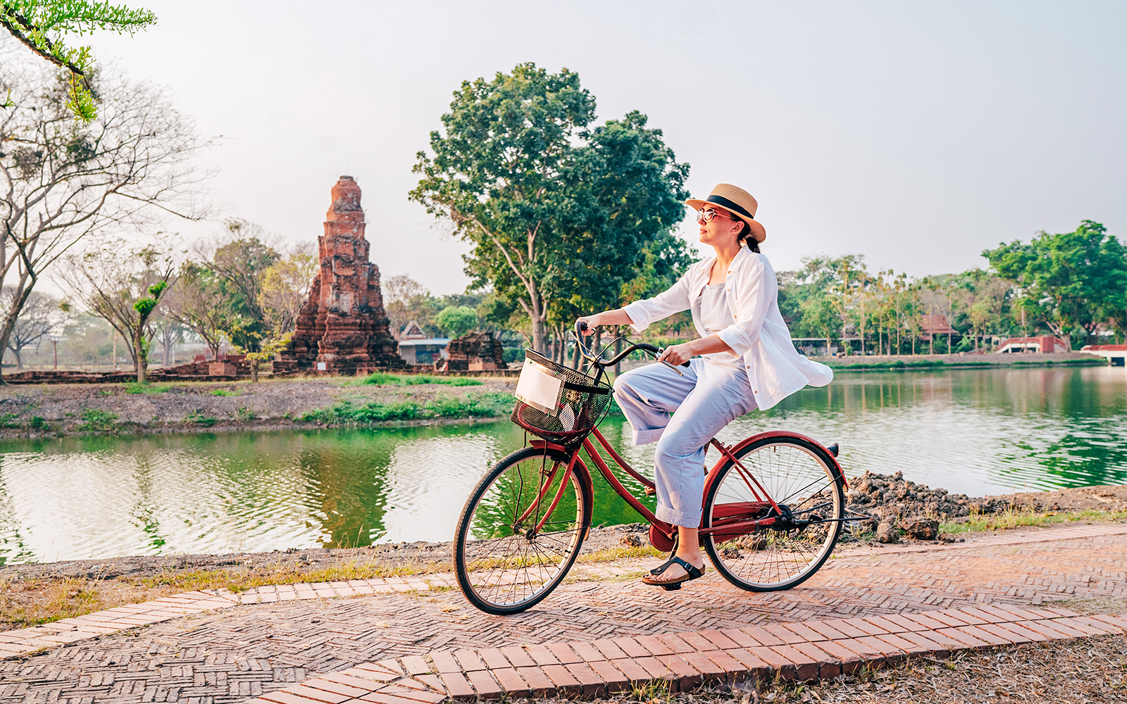 Woman cycling by ancient ruins in Ayutthaya Historical Park, Thailand.