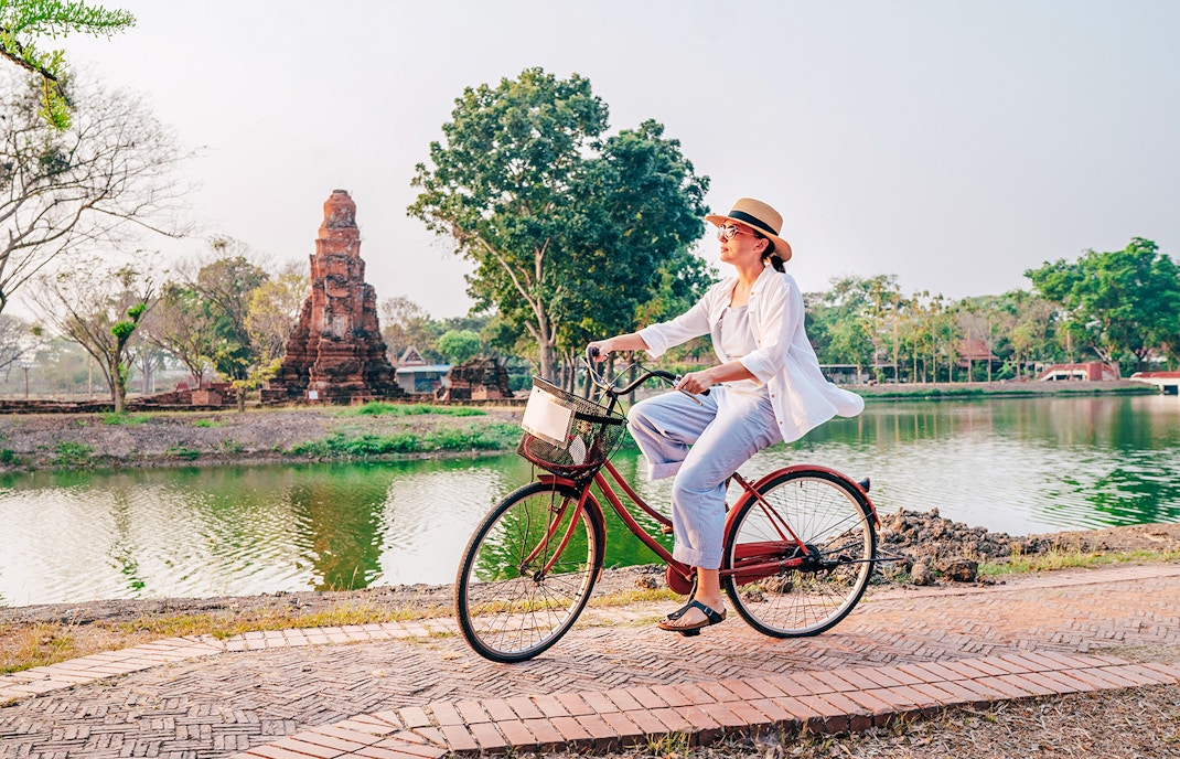Woman cycling by ancient ruins in Ayutthaya Historical Park, Thailand.