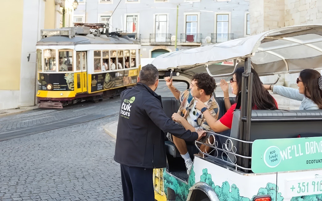Tourists in eco Tuk-Tuk with guide on Lisbon's Tram 28 route.