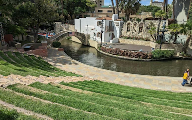Outdoor amphitheater by San Antonio River with stone bridge and stage, part of self-guided city game.