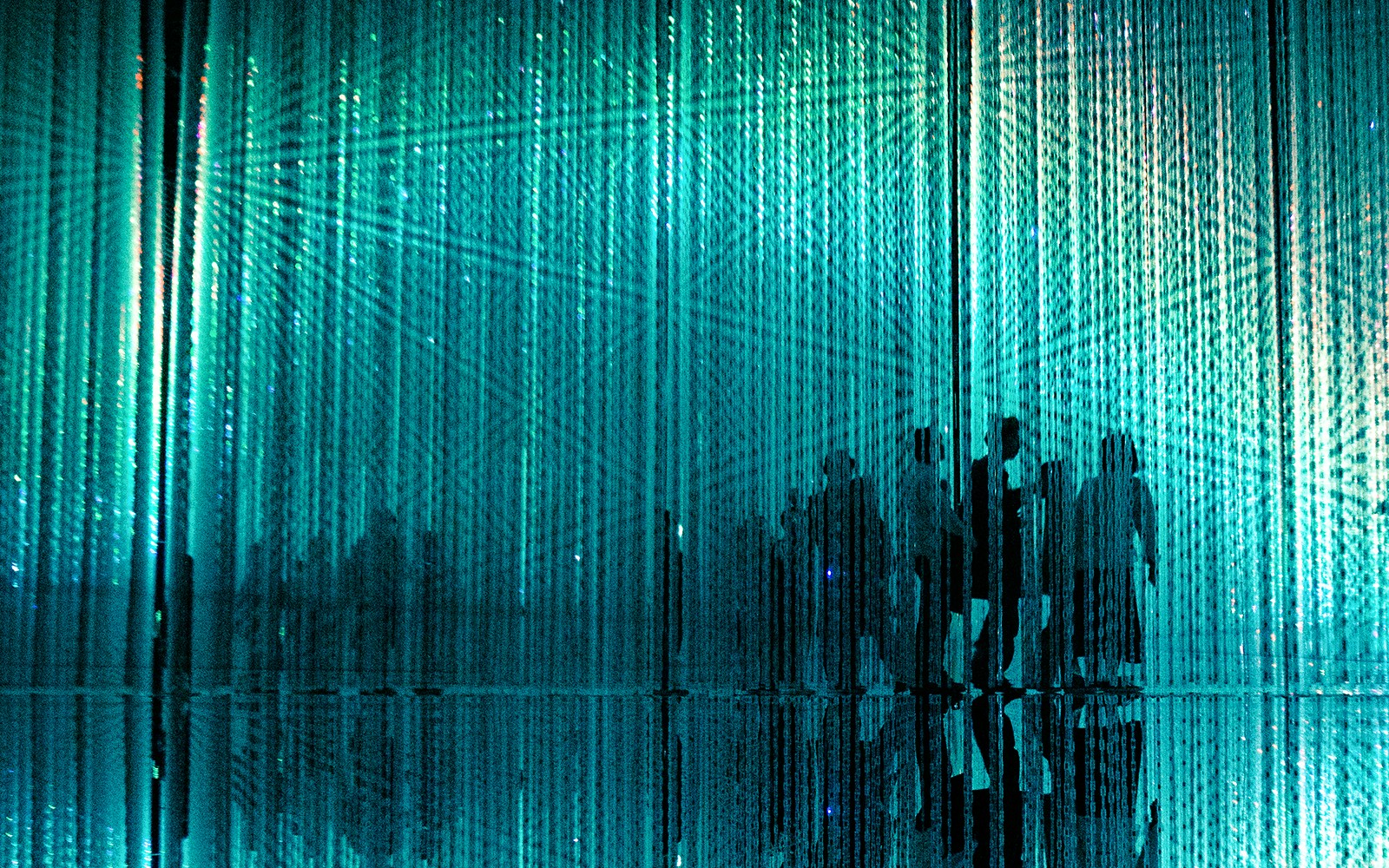 Visitors walking through immersive abstract art installation with blue light.