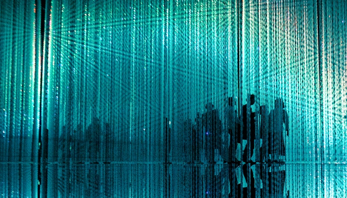 Visitors walking through immersive abstract art installation with blue light.