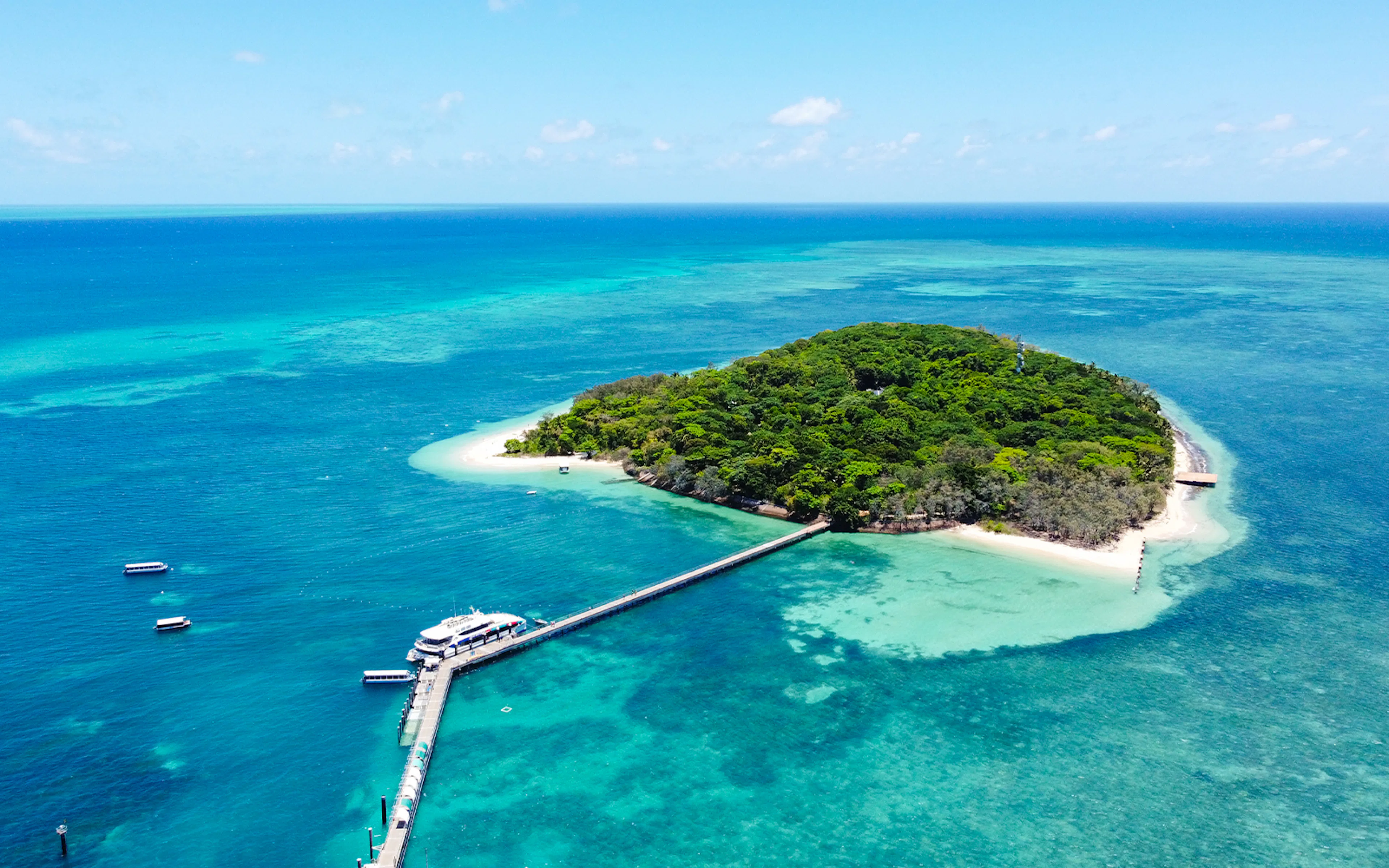 Tourists enjoying a Full Day Green Island Reef Catamaran Cruise in Cairns, Australia, with a view of the clear blue ocean and lush green island