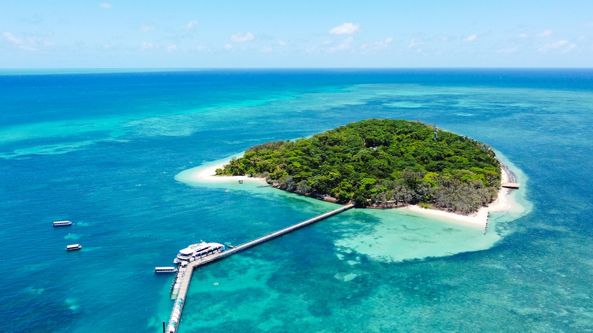 Tourists enjoying a Full Day Green Island Reef Catamaran Cruise in Cairns, Australia, with a view of the clear blue ocean and lush green island