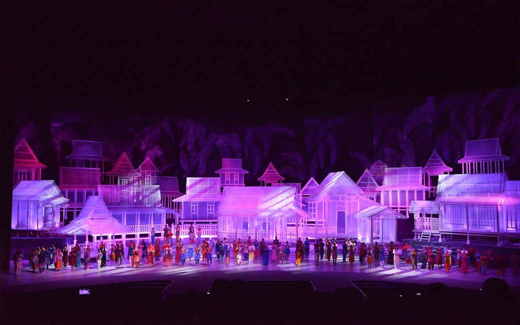 Traditional village scene with performers in colorful attire on stage, Kampung Scen.