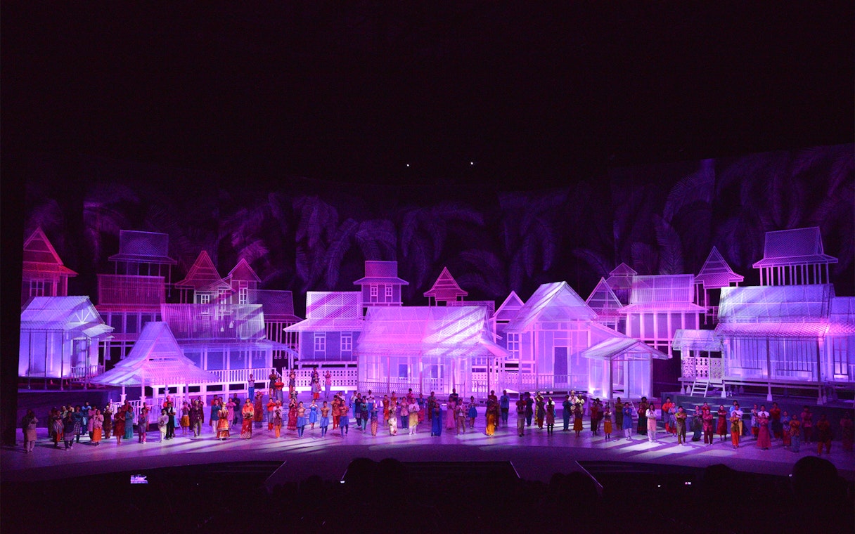 Traditional village scene with performers in colorful attire on stage, Kampung Scen.
