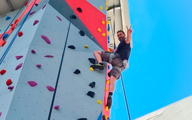 Person climbing an indoor rock wall during a bridge climbing experience.