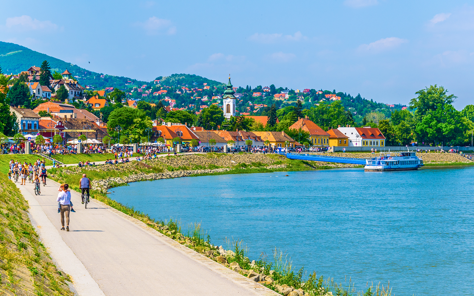 Riverside promenade in Szentendre, Hungary with people walking and cycling along the Danube River.