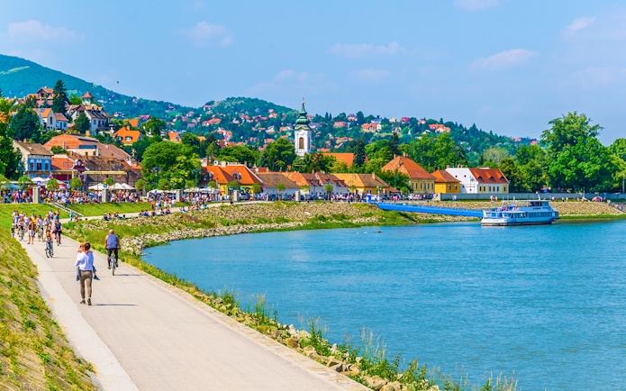 Riverside promenade in Szentendre, Hungary with people walking and cycling along the Danube River.