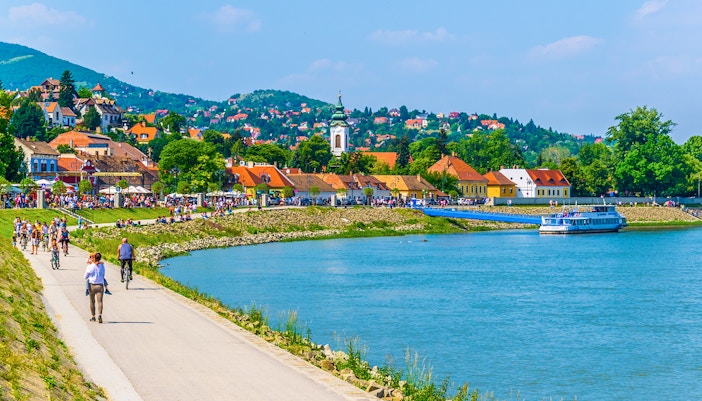 Riverside promenade in Szentendre, Hungary with people walking and cycling along the Danube River.
