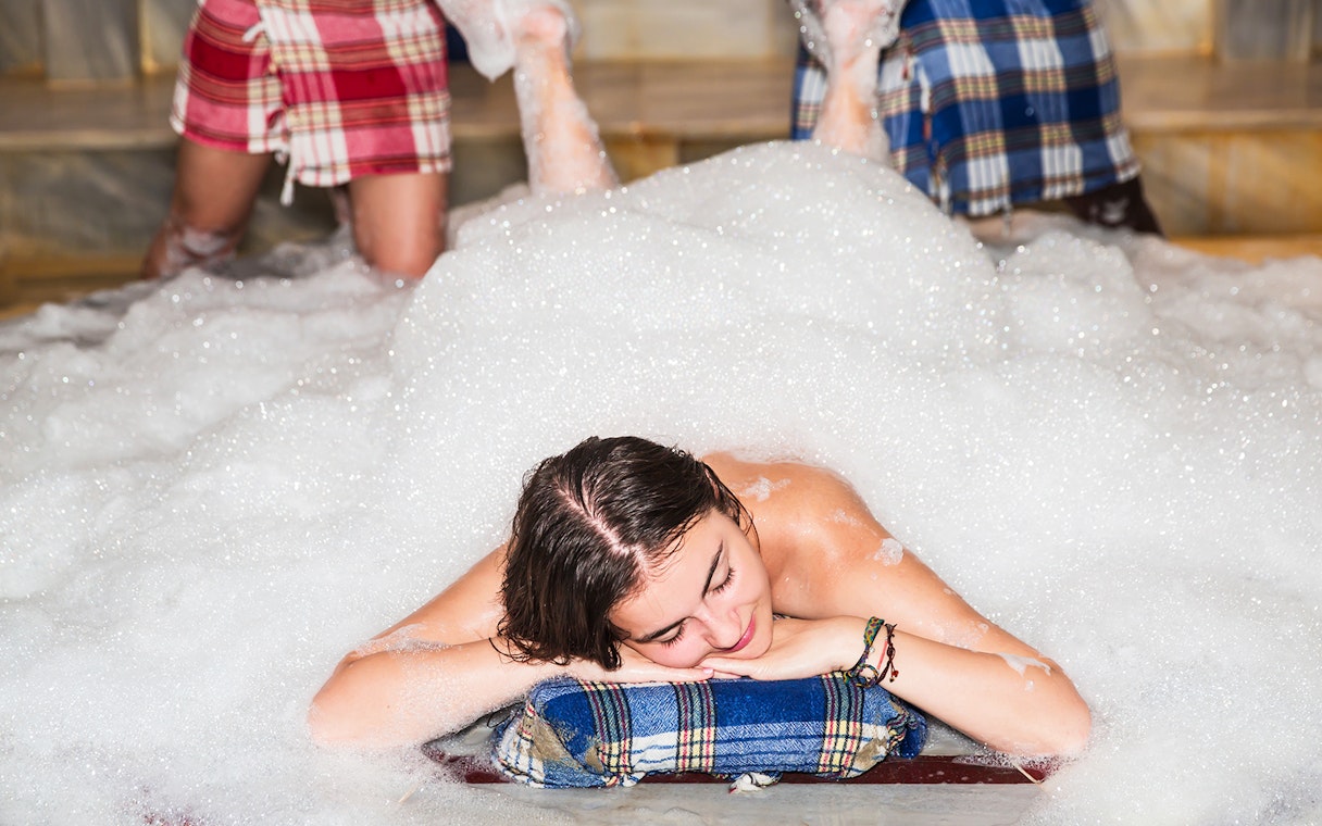 Traditional Turkish bath in Antalya with foam massage on marble surface.