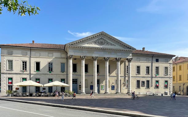 Neoclassical building in Como City with people walking and cycling nearby.