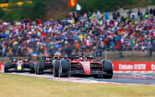 Formula 1 cars racing at the Hungarian Grand Prix with a crowd in the background.