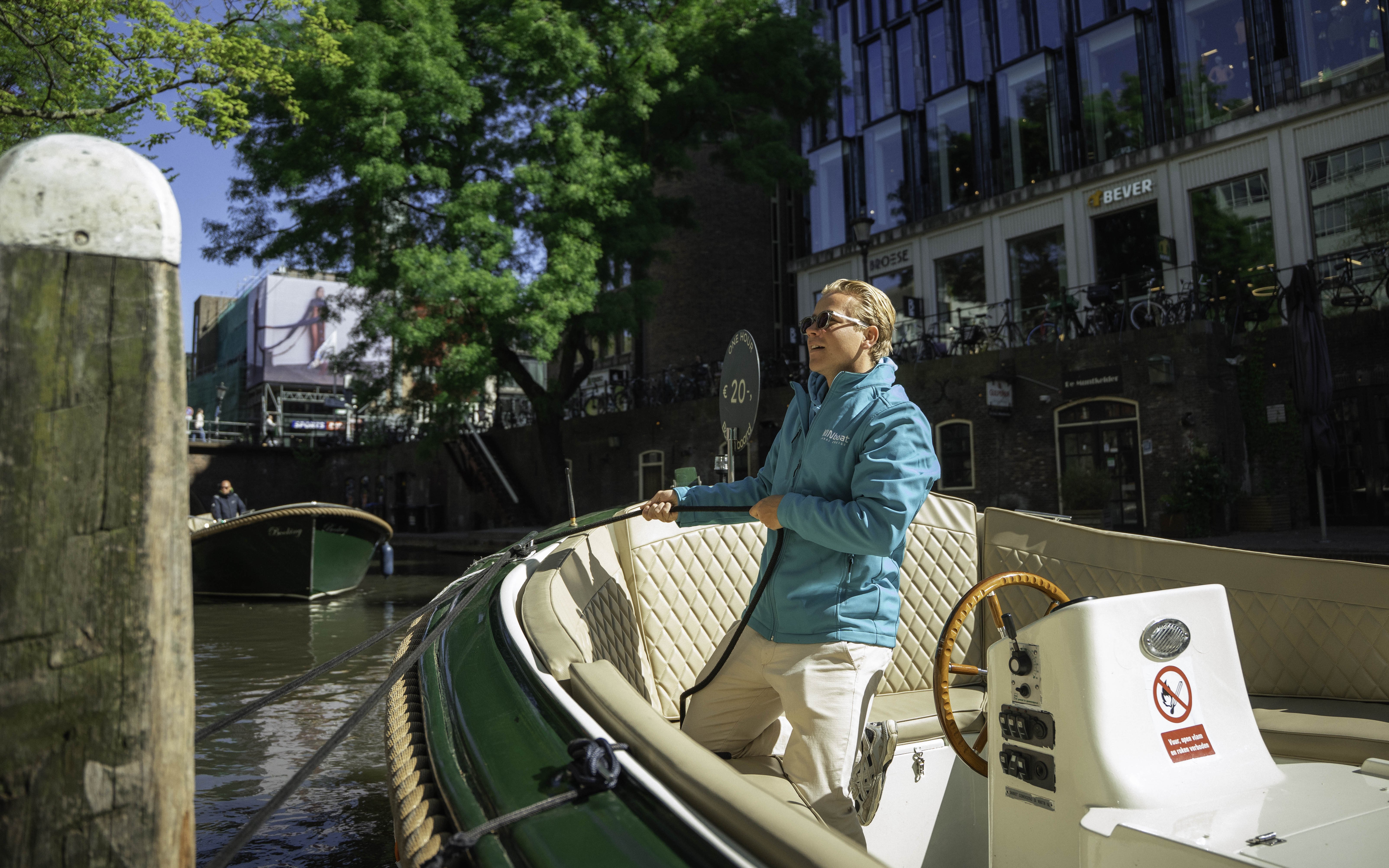 Boat captain steering a canal cruise in Utrecht, Netherlands, with city buildings in the background.