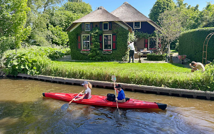 Kayakers paddle past a thatched cottage in Giethoorn during a self-guided boat rental tour.
