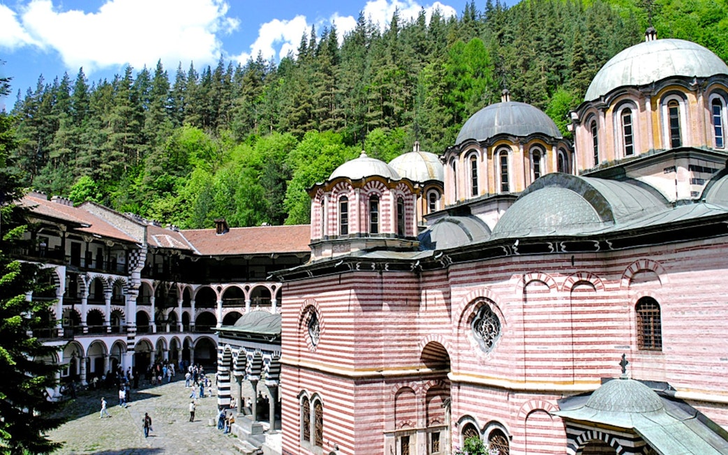 Rila Monastery courtyard with striped domes and forest backdrop, Bulgaria.