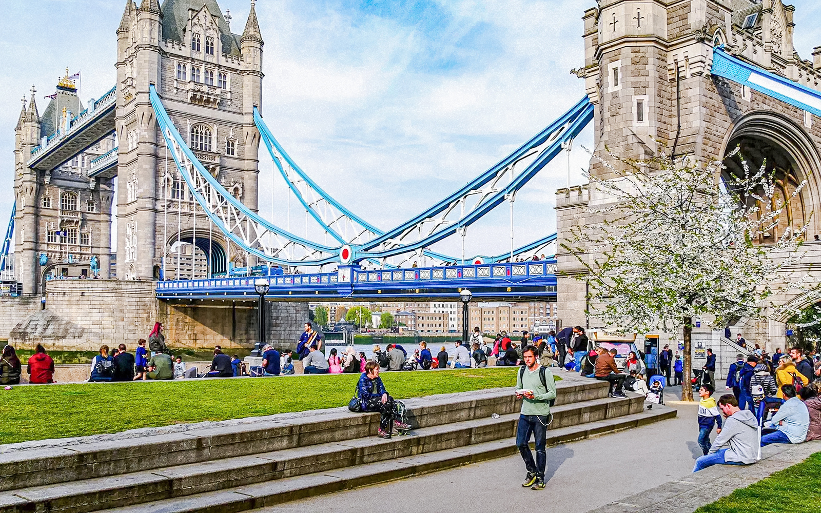 Tower Bridge in London with people relaxing on the grass nearby.