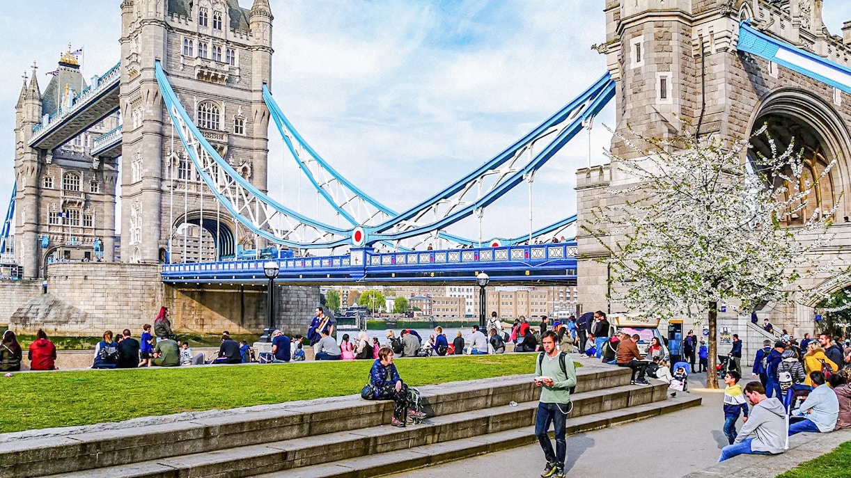 Tower Bridge in London with people relaxing on the grass nearby.