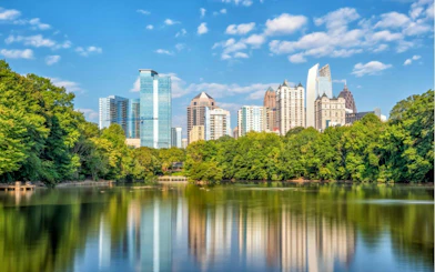 Atlanta skyline with skyscrapers and trees reflected in a lake, part of the self-guided city exploration game.