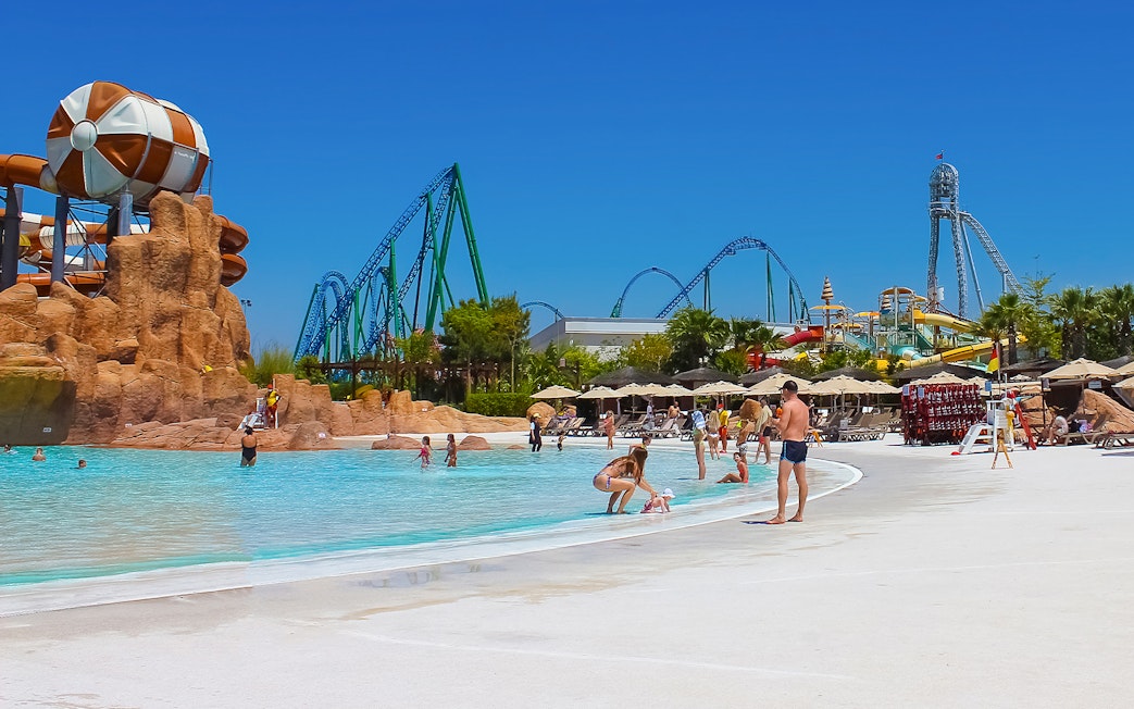 Visitors enjoying the pool at Land of Legends Theme Park, Antalya, with roller coasters in the background.