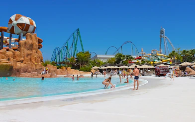 Visitors enjoying the pool at Land of Legends Theme Park, Antalya, with roller coasters in the background.