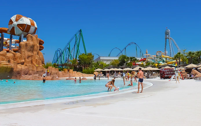 Visitors enjoying the pool at Land of Legends Theme Park, Antalya, with roller coasters in the background.