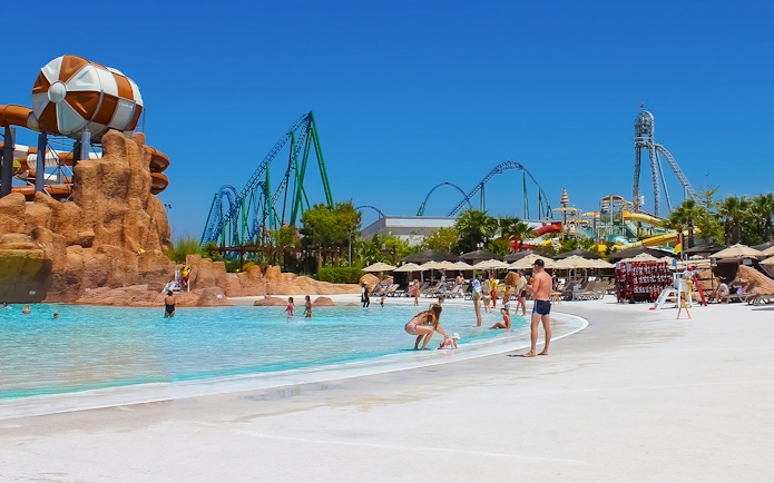 Visitors enjoying the pool at Land of Legends Theme Park, Antalya, with roller coasters in the background.