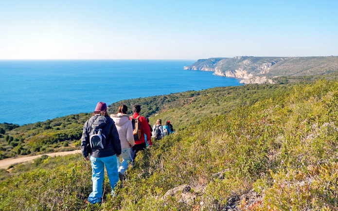 Hikers walking along a trail with ocean views at Arrábida Natural Park.