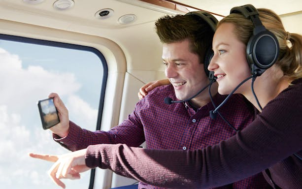 Couple enjoying a New York helicopter tour with headsets, taking photos.