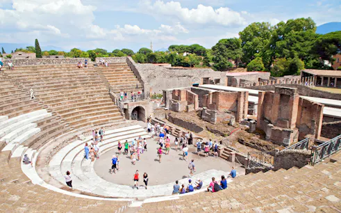 Tourists exploring the ancient amphitheater in Pompeii on a guided tour from Naples.
