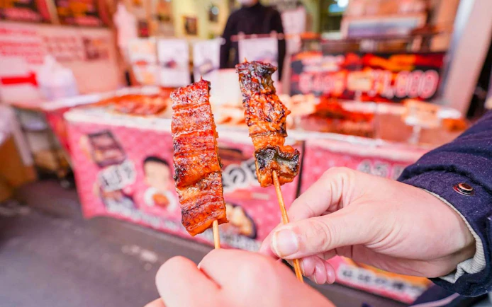 Tourists holding grilled skewers at Tsukiji Fish Market in Tokyo.