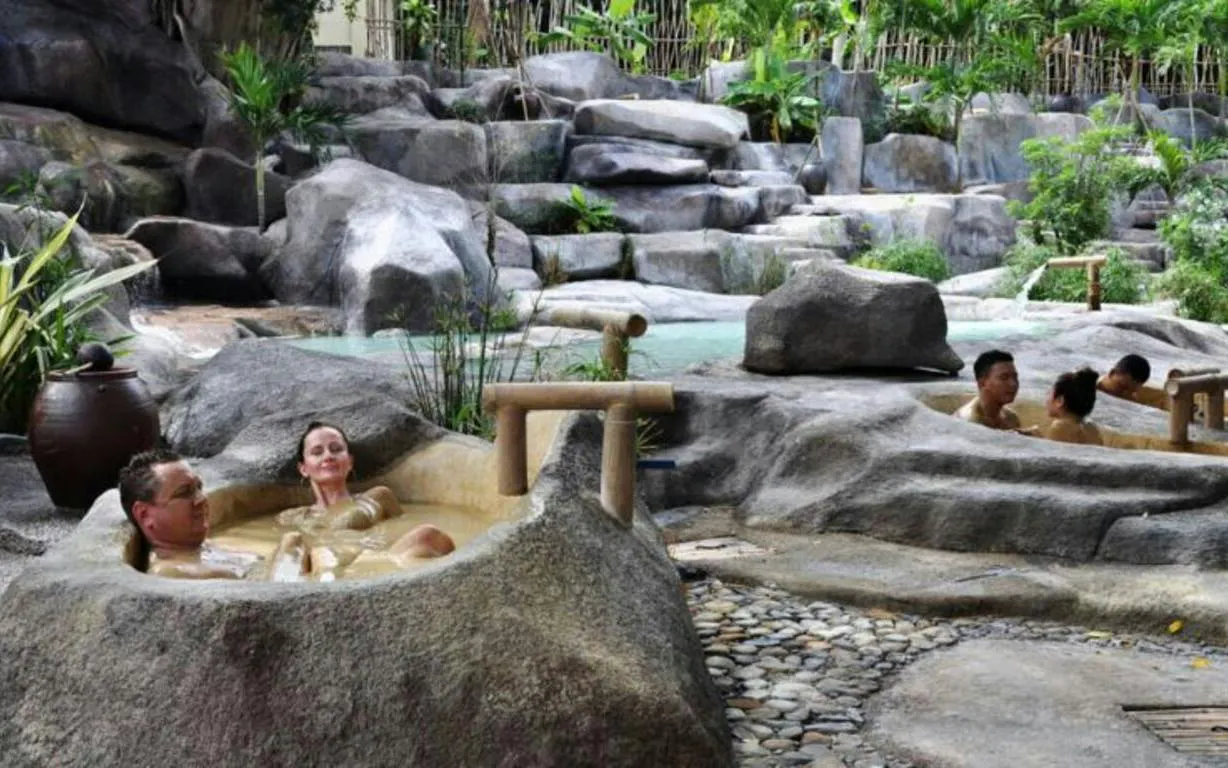 Adults relaxing in natural stone hot tubs surrounded by lush greenery at Cai River, Dubai.