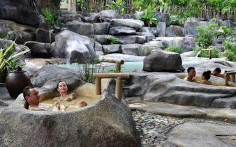 Adults relaxing in natural stone hot tubs surrounded by lush greenery at Cai River, Dubai.