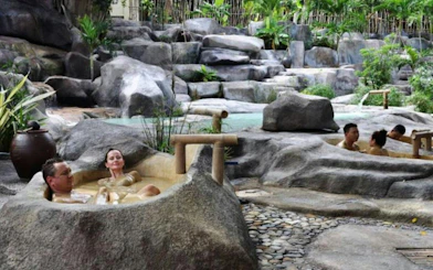 Adults relaxing in natural stone hot tubs surrounded by lush greenery at Cai River, Dubai.