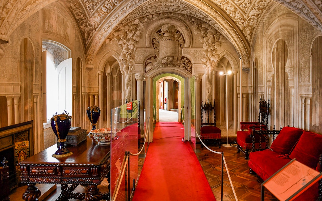 Interior hallway of Pena Palace in Sintra, Portugal, featuring ornate arches and red velvet seating.
