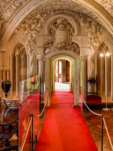 Interior hallway of Pena Palace in Sintra, Portugal, featuring ornate arches and red velvet seating.