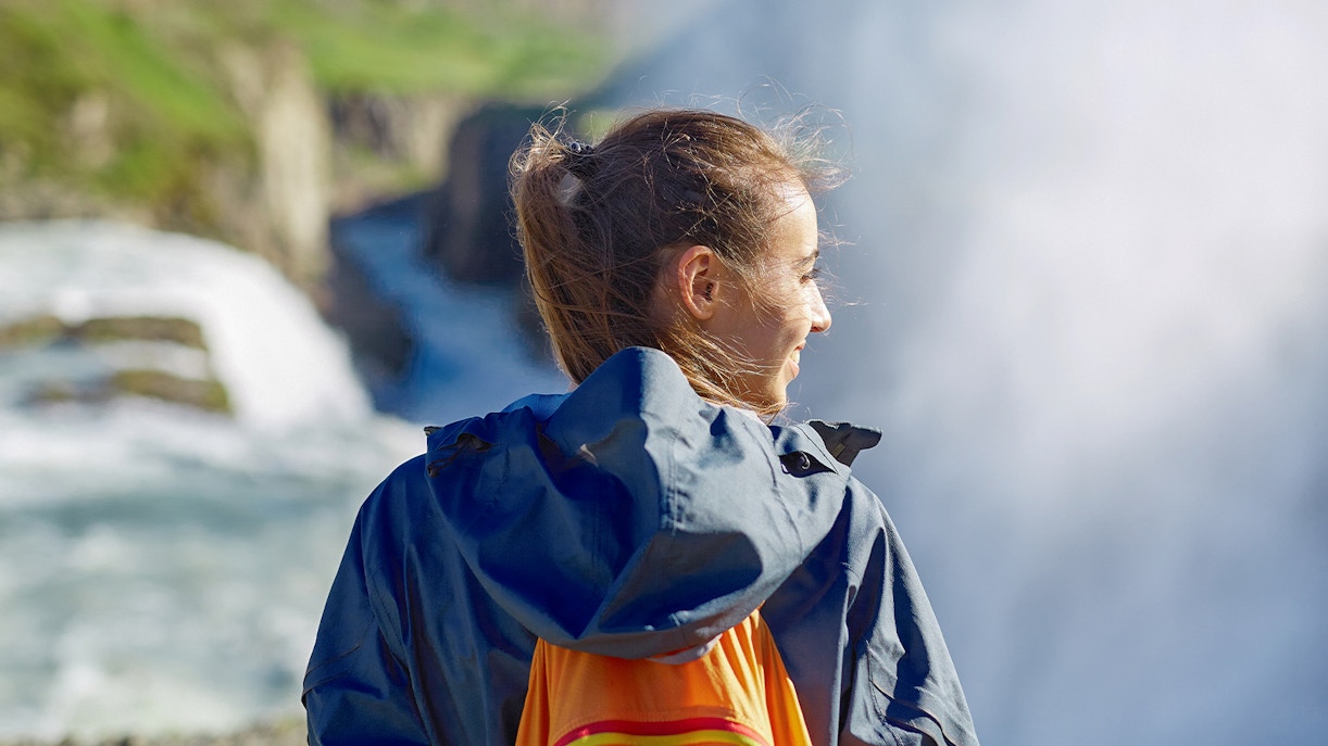 Woman in waterproof jacket near a waterfall, Iceland tour.