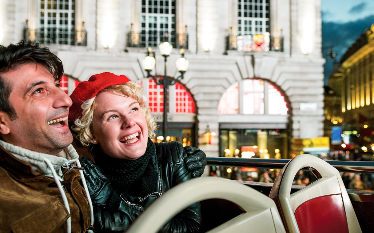 Couple enjoying London Christmas lights from open-top bus at night.