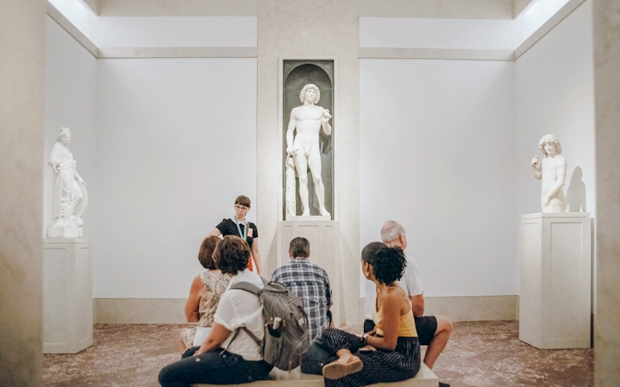 Tour group listening to guide near marble statue at Metropolitan Museum of Art.