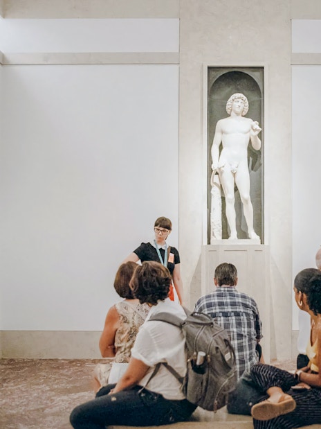 Tour group listening to guide near marble statue at Metropolitan Museum of Art.