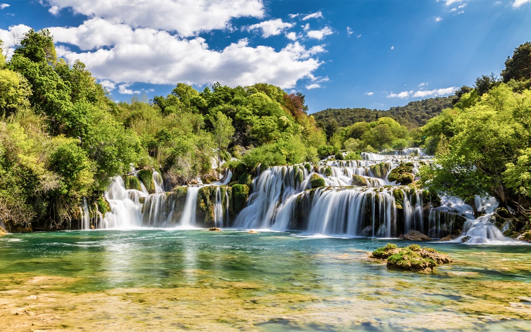 Waterfalls at Krka National Park, Croatia, surrounded by lush greenery under a blue sky.