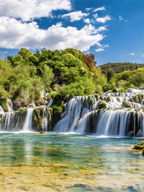 Waterfalls at Krka National Park, Croatia, surrounded by lush greenery under a blue sky.