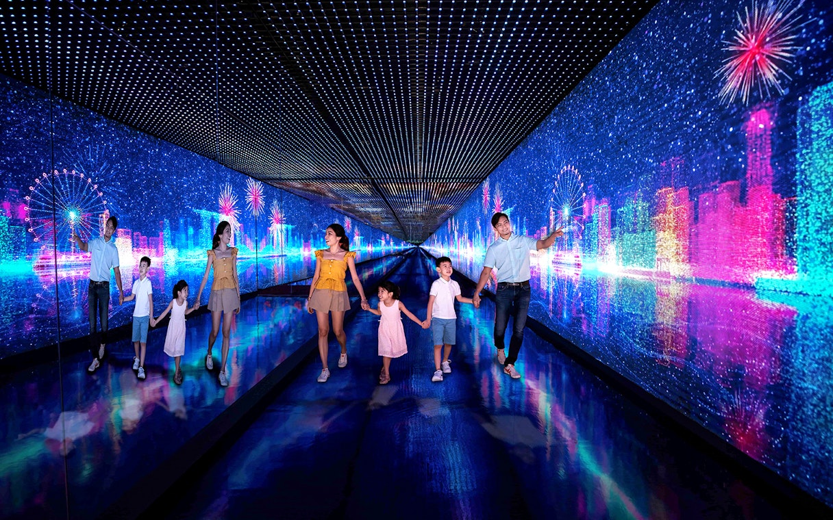 Families walking through the Time Capsule at Singapore Flyer with digital cityscape and fireworks.