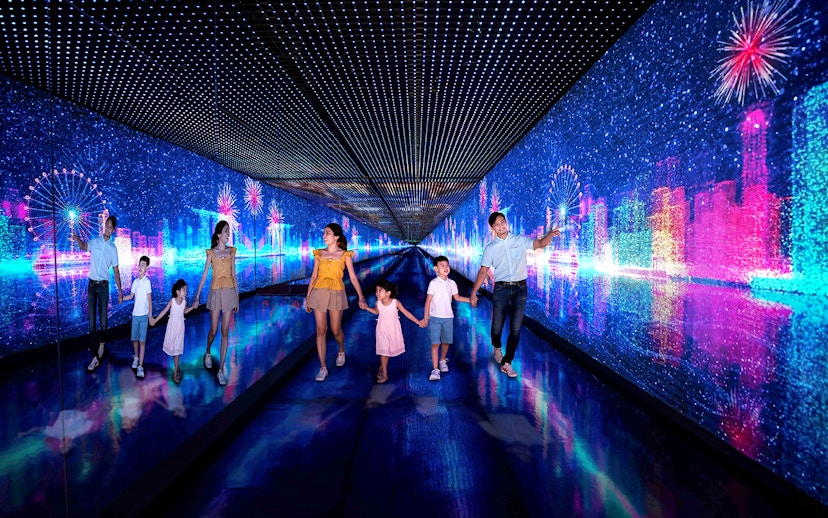 Families walking through the Time Capsule at Singapore Flyer with digital cityscape and fireworks.