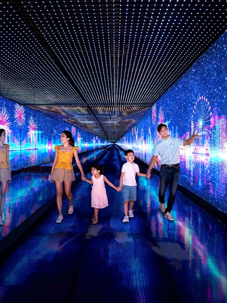 Families walking through the Time Capsule at Singapore Flyer with digital cityscape and fireworks.