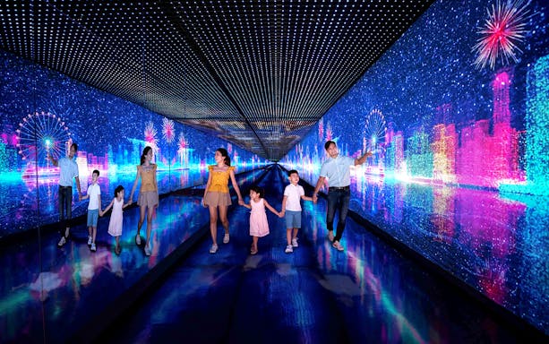 Families walking through the Time Capsule at Singapore Flyer with digital cityscape and fireworks.