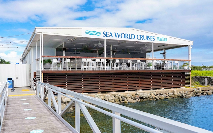 Pier leading to Sea World Cruises building with outdoor seating area.