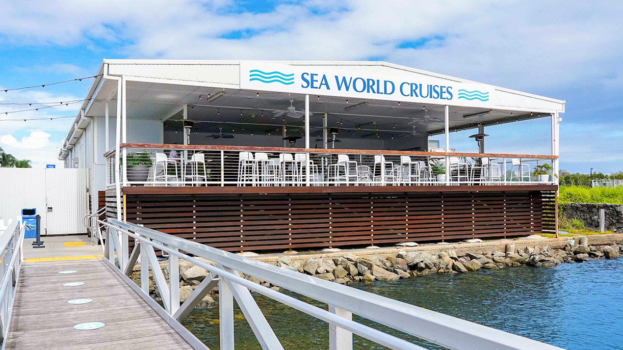 Pier leading to Sea World Cruises building with outdoor seating area.