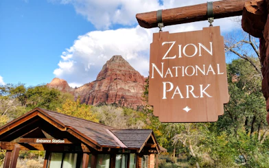 Zion National Park entrance sign with red rock formations in the background.